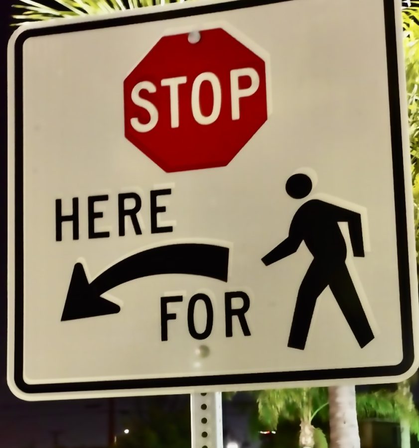 A stop sign signaling drivers to stop as pedestrians are crossing. Many reckless drivers ignore these signs and it can have a harmful outcome.